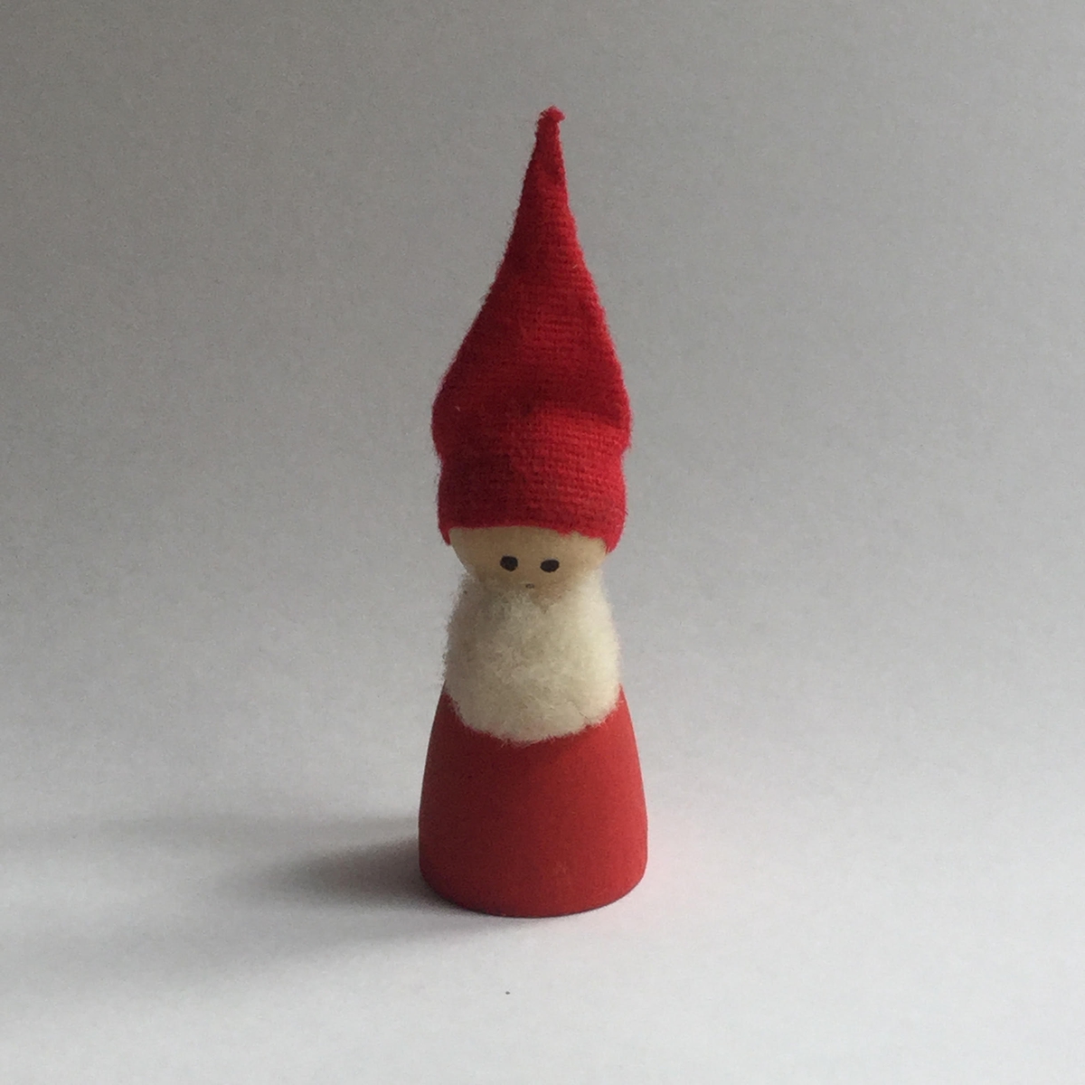 Tomte i trä med röd luva av tyg och vitt skägg av ull.