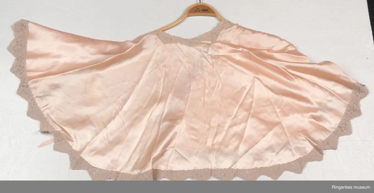 Klippet og sydd i halvsirkel, rundet halsutringning og åpen foran Kantet med bred blonde . .A- har silkebånd på hver  side. B - har  en liten trykknapp nede på venstre side.