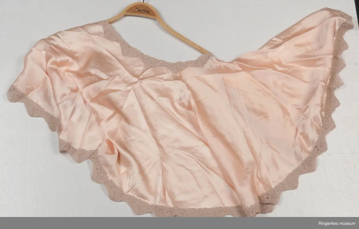 Klippet og sydd i halvsirkel, rundet halsutringning og åpen foran Kantet med bred blonde . .A- har silkebånd på hver  side. B - har  en liten trykknapp nede på venstre side.