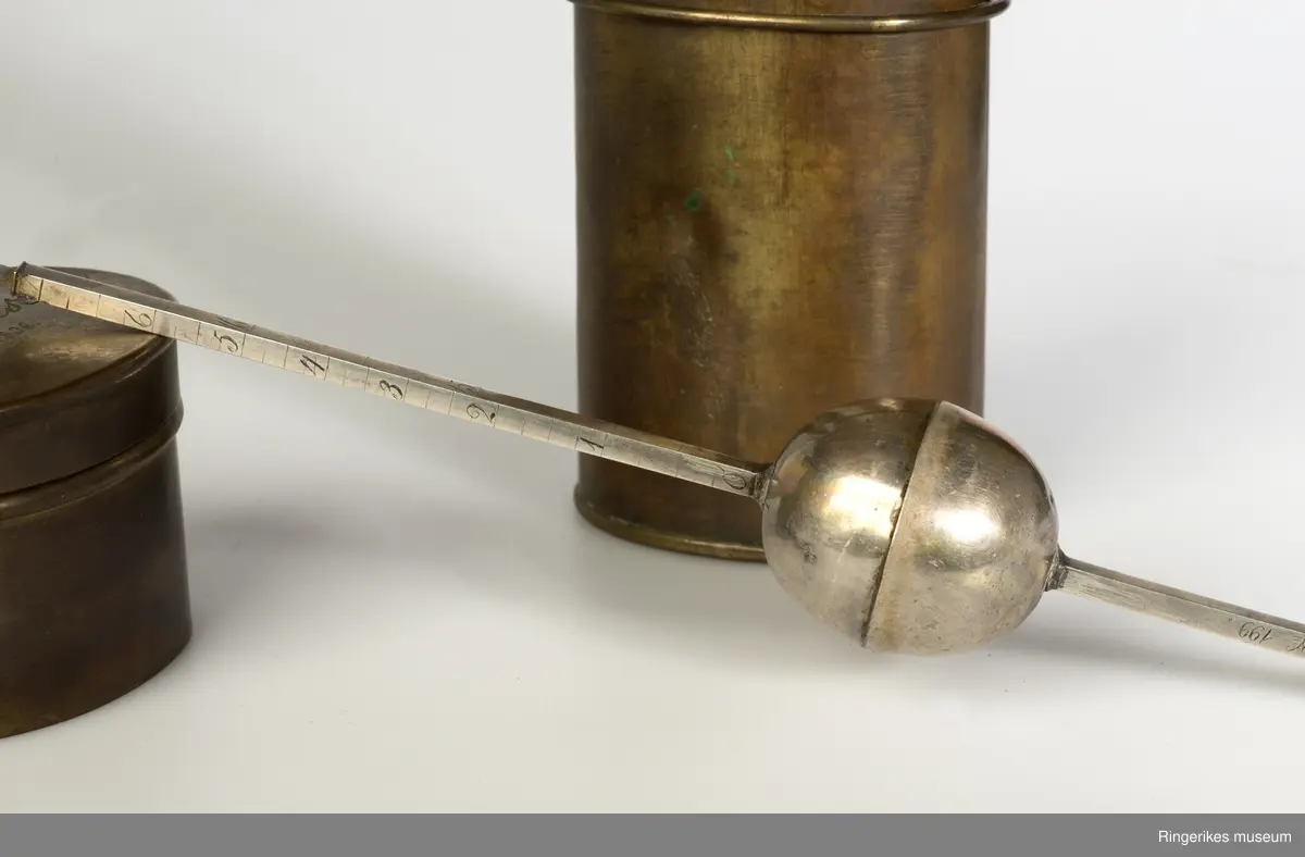 A: hylse eller etui med lokk, sylinderform, lokk med feste og ring for å henge på til annet måleutstyr og lignende. Lokket slutter tett til. 
B: måleinstrument, opprinnelig bruk og funksjon ukjent.Gravering av tallskala både på målestang og kule gir en viss informasjon. Stangen har et lite sirkelformet metall i den ene ende og et sylinderformet propp i den andre. Den er skrudd inn i målestangen.