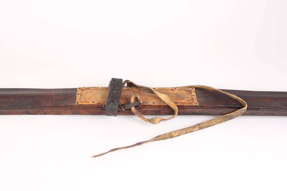 Et par ski, trolig i ask. Framskien er avsmalnende og bakskien er jevnbred. Skiens forende har en profilert tupp, type nese. Bakskien ender i en oppbøyd spiss. Skiens overside har en møneformet rygg med hulkil, og en dyp midtrand under. 
Bindingen er i skinn, festet med tau. Fotstegplaten i bjørkenever er festet med metallstifter.