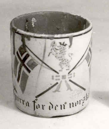 To norske flagg der stengene er holdt sammen med ei sløyfe. Over denne står ei løve med krone og øks, og dette midtmotivet er innramma av greiner med eikeløv og eikenøtter.