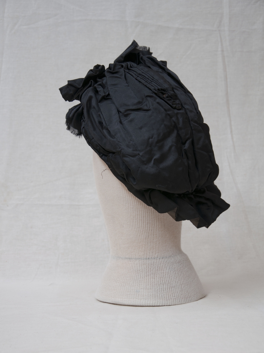 Svart, brodert, handsydd kyse med knyteband.
Sydde legg, perlebrodert.