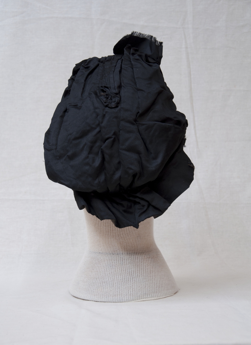 Svart, brodert, handsydd kyse med knyteband.
Sydde legg, perlebrodert.