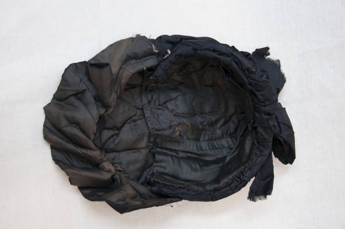 Svart, brodert, handsydd kyse med knyteband.
Sydde legg, perlebrodert.