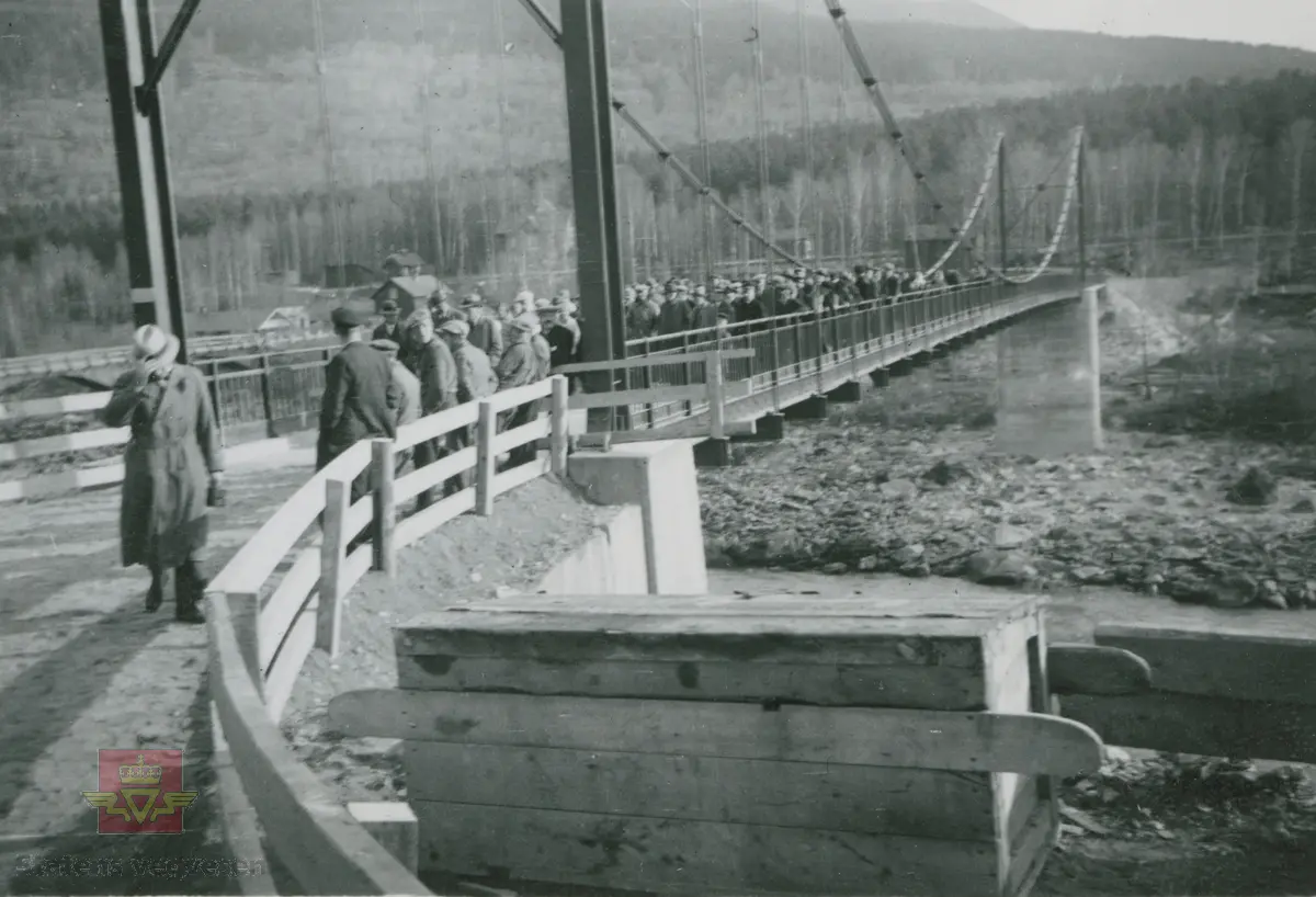 Album fra 1929-1943.  Kolobrua  på Sjoa over Gudbrandsdalslågen. Sannsynligvis er det åpning av nybygd bru  høsten 1937. Foran på bildet står ei transportkasse. Sjoa stasjon vises  i bakgrunnen.  Skilt på brua med følgende tekst: " Største lovlege last pr. aksel eller einskild  slede 5000 kg. Køyrereidskap medrekna."