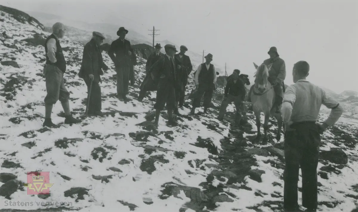 Album fra 1929-1943. Fra befaring over Sognefjell  1935, med samme gruppe menn som på bilde NVM 00-F-32793 og NVM 00-F-32796.  Fra venstre overingeniør Knud Knudsen og vegdirektør Andreas Baalsrud.  Overingeniør Carl Crøger med sixpence og ryggsekk står midt på bildet , de andre personene er ukjent.