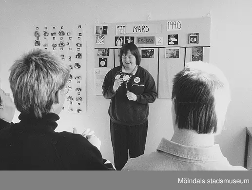 En ung kvinna står framför en vägg och håller i ett kort. Okänd person och årtal.