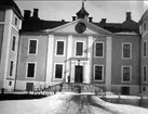 Vid Strömsholm slott. På skylten över entrén står HERS= Hedvig Eleonora Regina Swecia. Av många elever uttytt: Helvetes elegant ridskola (vid gott humör) eller Här eldas rysligt sällan (vid dåligt humör). Strömsholm 1910-11.