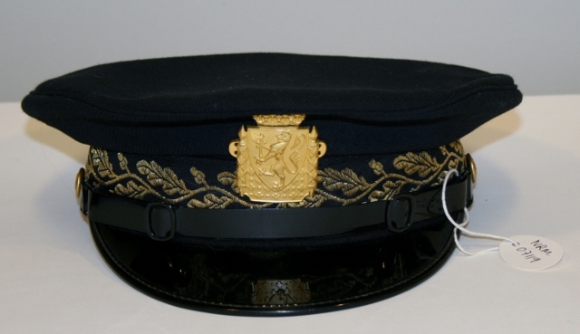 Uniform for politinspektør etter 1963-reglement med merking etter 1977-reglement. Helårsuniform M/1963 med skjorte, langbukse, belte, helårskappe og jakke. Skyggelue med gullbrodert bånd, loslue og båtlue M/1967. Kappen og jakken har skulderklaffer av flettede gullsnorer med to sølvstjerner og festeknapp i gullbroderi. Skjorten har en enklere skulderklaff med to gule render og to sølvstjerner. Det følger med et ekstra enkelt lærbelte og et ekstra sett skulderklaffer til skjorte. Plaggene har gullfargede løveknapper.