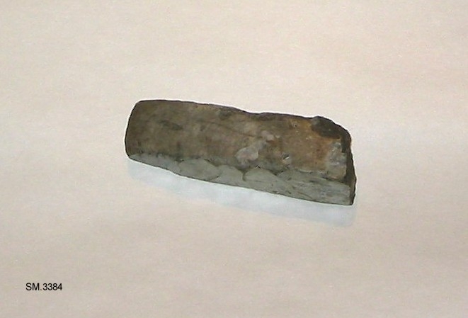 Fragment av meisel av flint, bare eggpartiet bevart. Formen synes å likne Rygh 18 eller Gjessing: Rogalands steinalder, fig.105, med slipt, slank egg. Tverrsnittet kvadratisk. Fragmentet er laget av gråhvit flint, med sprukket overflate, synes å være ildskjørnet.