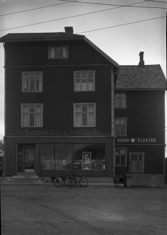 Sortland Bok & Papirhandel i Heidenstrømgården (Bokhandlergården) ca. 1950. Bygningen ble satt opp i 1920 av Reidar Heidenstrøm, som var direktør ved Vesteraalens Hermetikkfabrikk. Den ble brukt til bolig og ulike forretninger. Bl.a. hadde fotograf Lind atelier der.