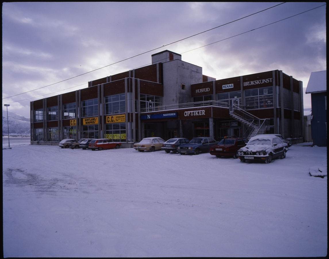 Forretningsbygg på sørsida av torget på Sortland, 1984. Her holdt blant annet Sortland bibliotek til i 2. etasje fra 1986 til 2014, tannlegekontor i 3. etasje og optiker i 1. etasje. Bygget ble senere bygd sammen med det som ble Sortland Storsenter. Like utenfor venstre bildekant lå fergekaia på Sortland, som var i bruk til 1983.