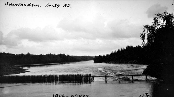 Nåledam ved Svanfoss i Fenstad i Nes kommune på Øvre Romerike i Akershus fylke. Denne dammen hevet vannspeilet i den ovenforliggende delen av elva Vorma og bidro dermed til at det ble mulig for mjøsbåtene å gå til Sundet i Eidsvoll kommune. I 1929, da dette fotografiet ble tatt, var Svanfossdammen en såkalt «fermettedam», en 3,2 meter høy stålkonstruksjon som bar ei gangbru, der fløterne kunne gå når de skulle «sette dammen» (stenge) eller «sprette» (åpne) den. Dette ble gjort ved hjelp av «nåler», plank som ble stukket mot strømmen, slik at den lå an mot en terskel i botnen av elveløpet og mot gangbrua.  Disse nålene ble satt tett i tett, slik at de sammen dannet en vegg mot vannet.  Når dammen ble åpnet, brukte karene små kjetting- eller taustubber med ei jernnål i enden, som ble tredd gjennom hull i den øvre delen av nålene, og trakk til. Da dette fotografiet ble tatt var nåledammen ved Svanfoss bare delvis stengt. Bildet er tatt i medstrøms retning, fra dammen mot det nedenforliggende elveløpet, hvor strømmen var stridere.