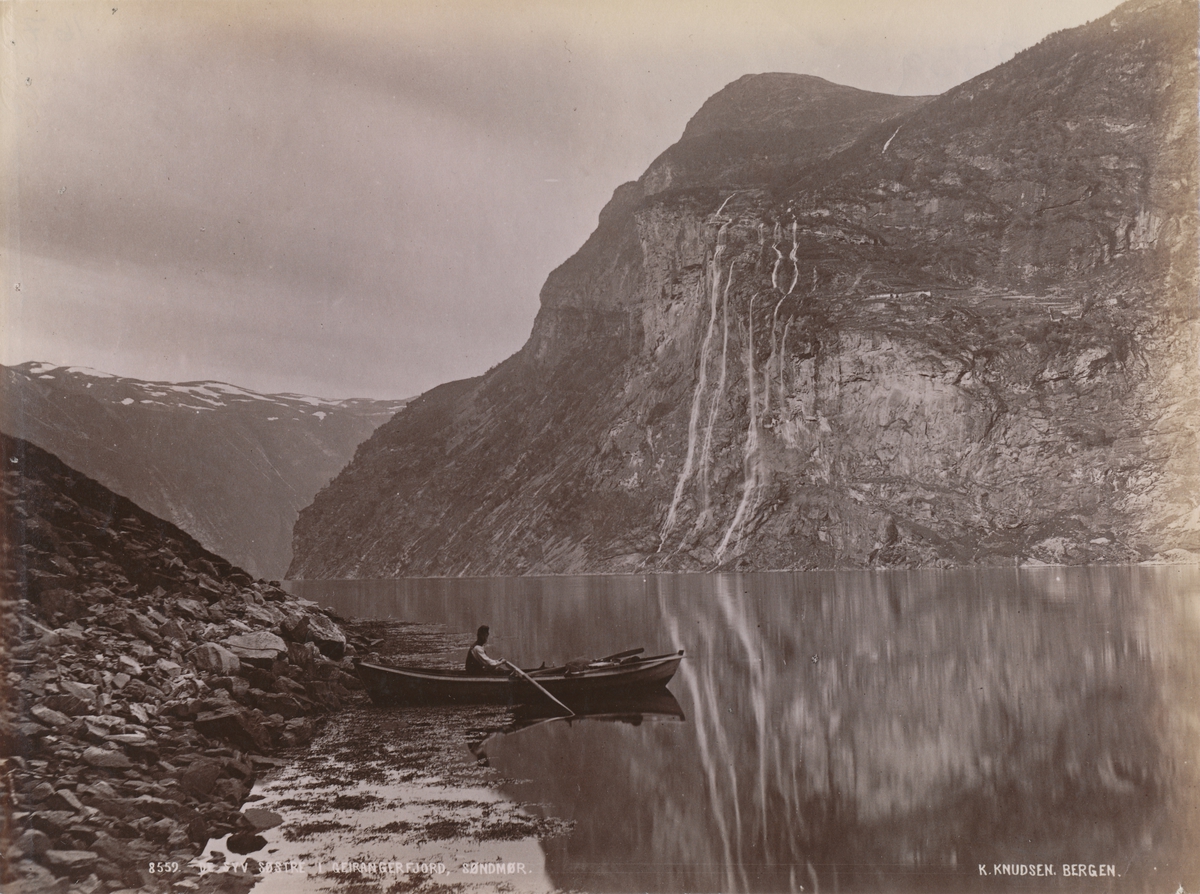 Mann i båt foran fossen "De syv søstre" i Geirangerfjorden.