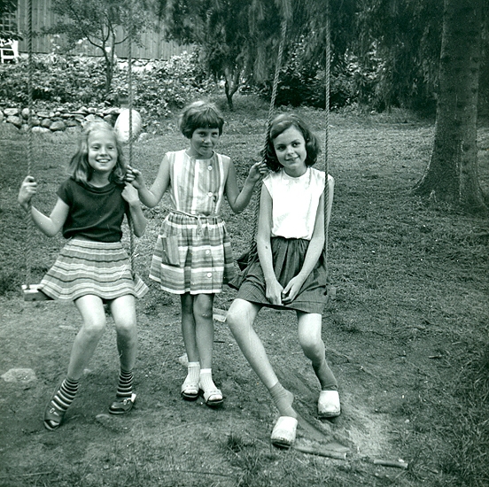 Sommaren 1962 hos Agneta Turesson. Veronika i mörkröd topp med båtringning och hemmastickad grå yllekjol med ränder i rött, gult, vitt
Agneta T. i mitten min "bästis" i flera år. Elisabeth Madgård i diadem och vit blus, blå kjol med sparveck (skulle släppts ner) och träskor. 
(Fotograf kan vara Gertrud.)