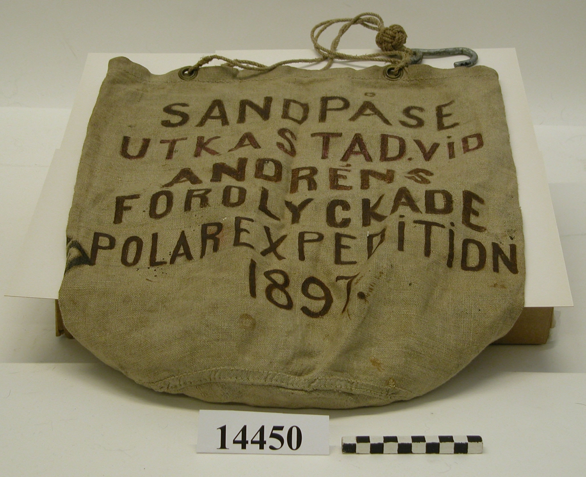 Handsydd, upptill försedd med fyra kauser. I vardera kausen är fastsatt en tregarnslina. Förenade med krok av galvaniserat järn.

Märkning: "Andrens polarexpedition 1897 samt "Sandpåse utkastad vid Andrens (sic!)
förolyckade polarexpedition 1897."