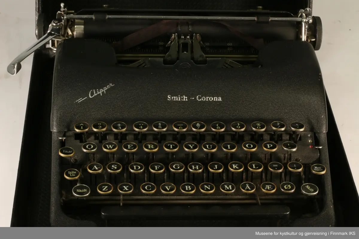Sort reiseskrivemaskin i koffert. Av merket Smith-Corona, modell Clipper med norsk tastatur.

Kofferten er sort, har håndtak i plast og lås av metall (nøkkel mangler).