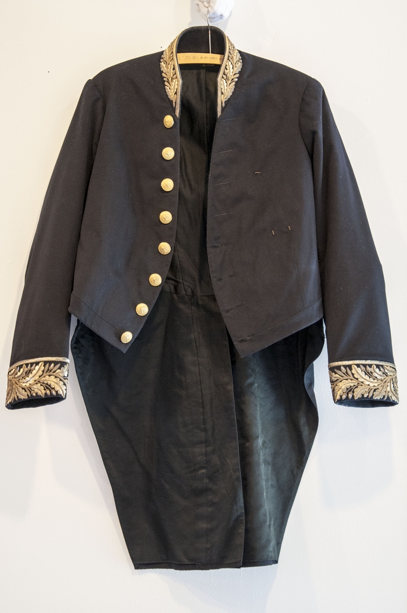 Stoffet i uniforma er av svart, fint klede. Kjolen (jakka) er figursydd. Bak har jakka to lange "skjøt" dekorert med åtte gullknappar med løvemotiv. På framstykket åtte gullknappar med løvemotiv, fire til knapping og fire til dekor. Jakka har oppståande krage med gullmetall-dekor, same dekoren er og nede på ermane. Jakken er fora med silke- og bomullsstoff.