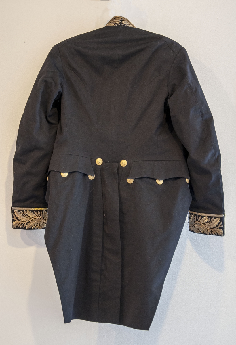 Stoffet i uniforma er av svart, fint klede. Kjolen (jakka) er figursydd. Bak har jakka to lange "skjøt" dekorert med åtte gullknappar med løvemotiv. På framstykket åtte gullknappar med løvemotiv, fire til knapping og fire til dekor. Jakka har oppståande krage med gullmetall-dekor, same dekoren er og nede på ermane. Jakken er fora med silke- og bomullsstoff.