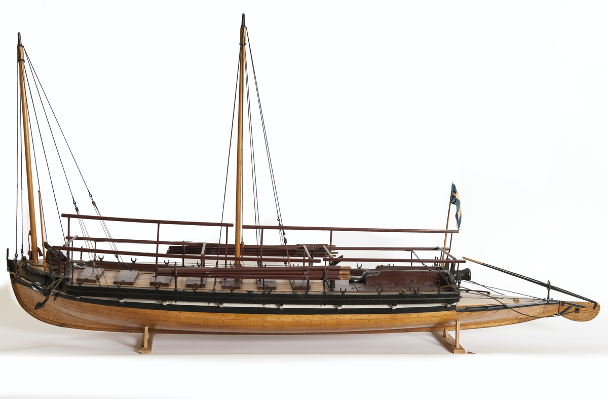Båtmodell, däckad kanonjolle 1788 års typ. Riggad med två loggertsegel, flagga och spel, vimpel och gösstake. Bordlagd på spant, kravell med inredning. Utdragen akter, tältstomme. 10 par årtullar, 20 st åror, 1 styråra. Roder med rorpinne. Fernissad med svart/vit reling. Bruna åror, däcksluckor och lavetter. 2 träkanoner. 2 fernissade skrå.
Nytt skrå 1938. En grov kanon akterut, en nicka förut. En man vid åran.