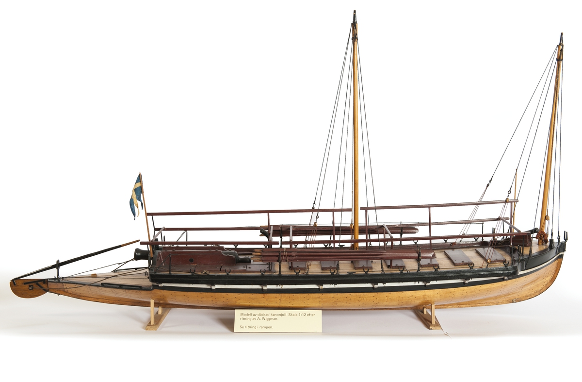 Båtmodell, däckad kanonjolle 1788 års typ. Riggad med två loggertsegel, flagga och spel, vimpel och gösstake. Bordlagd på spant, kravell med inredning. Utdragen akter, tältstomme. 10 par årtullar, 20 st åror, 1 styråra. Roder med rorpinne. Fernissad med svart/vit reling. Bruna åror, däcksluckor och lavetter. 2 träkanoner. 2 fernissade skrå.
Nytt skrå 1938. En grov kanon akterut, en nicka förut. En man vid åran.