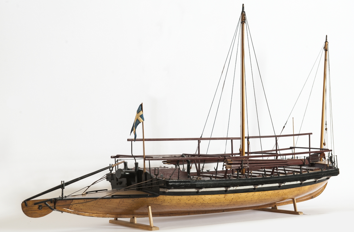 Båtmodell, däckad kanonjolle 1788 års typ. Riggad med två loggertsegel, flagga och spel, vimpel och gösstake. Bordlagd på spant, kravell med inredning. Utdragen akter, tältstomme. 10 par årtullar, 20 st åror, 1 styråra. Roder med rorpinne. Fernissad med svart/vit reling. Bruna åror, däcksluckor och lavetter. 2 träkanoner. 2 fernissade skrå.
Nytt skrå 1938. En grov kanon akterut, en nicka förut. En man vid åran.