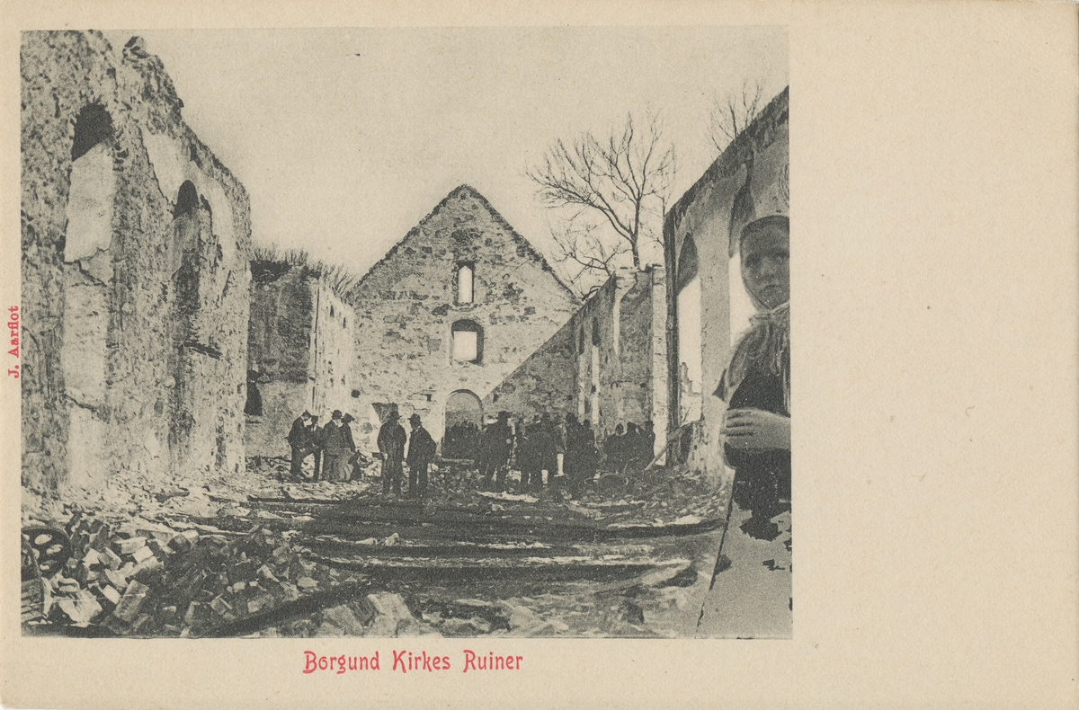 Borgund kirke i ruiner etter brannen 1904. Motiv fra innsiden der en gruppe mennesker er samlet.