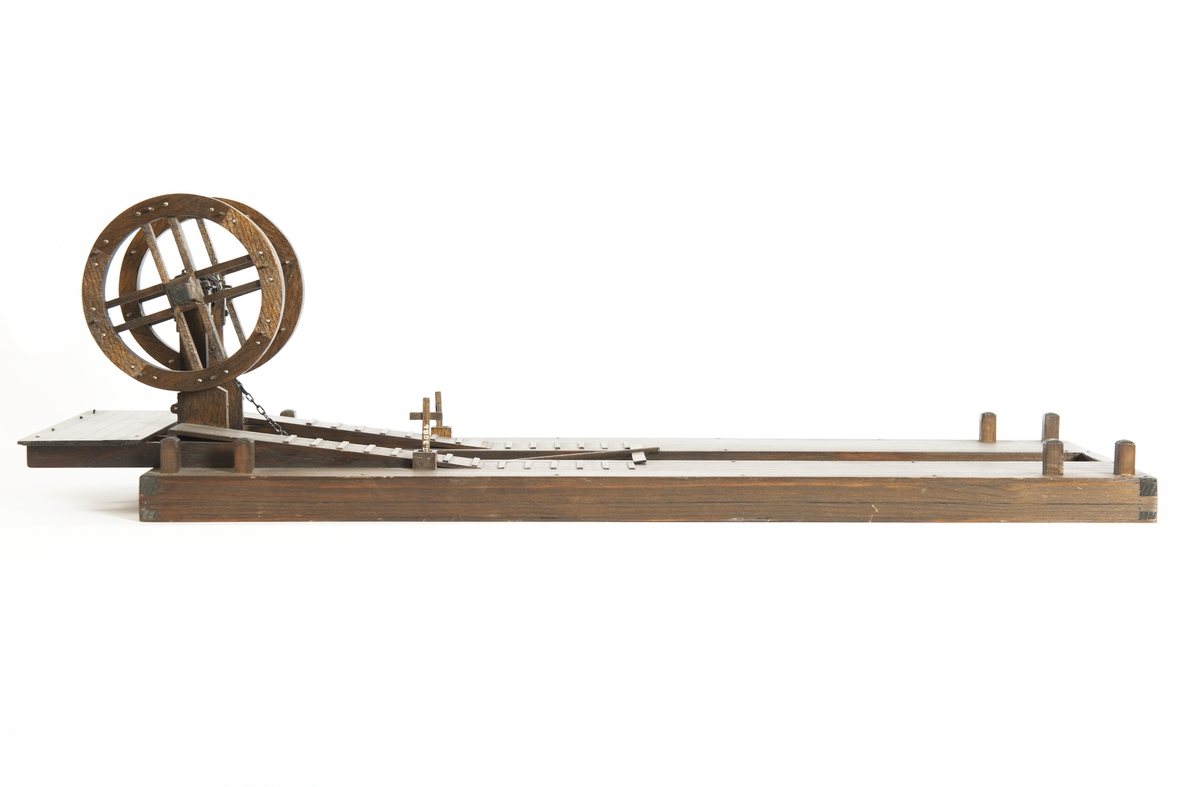 Modell av furu, betsad. Flotte, tudelad, jämte mudderskopa och liggande spel. Dubbla pollare i alla hörn samt två pumpar på flotten.