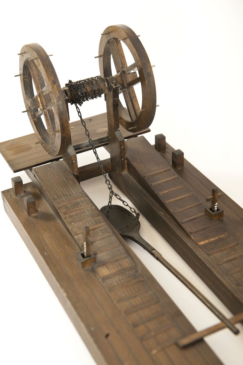 Modell av furu, betsad. Flotte, tudelad, jämte mudderskopa och liggande spel. Dubbla pollare i alla hörn samt två pumpar på flotten.