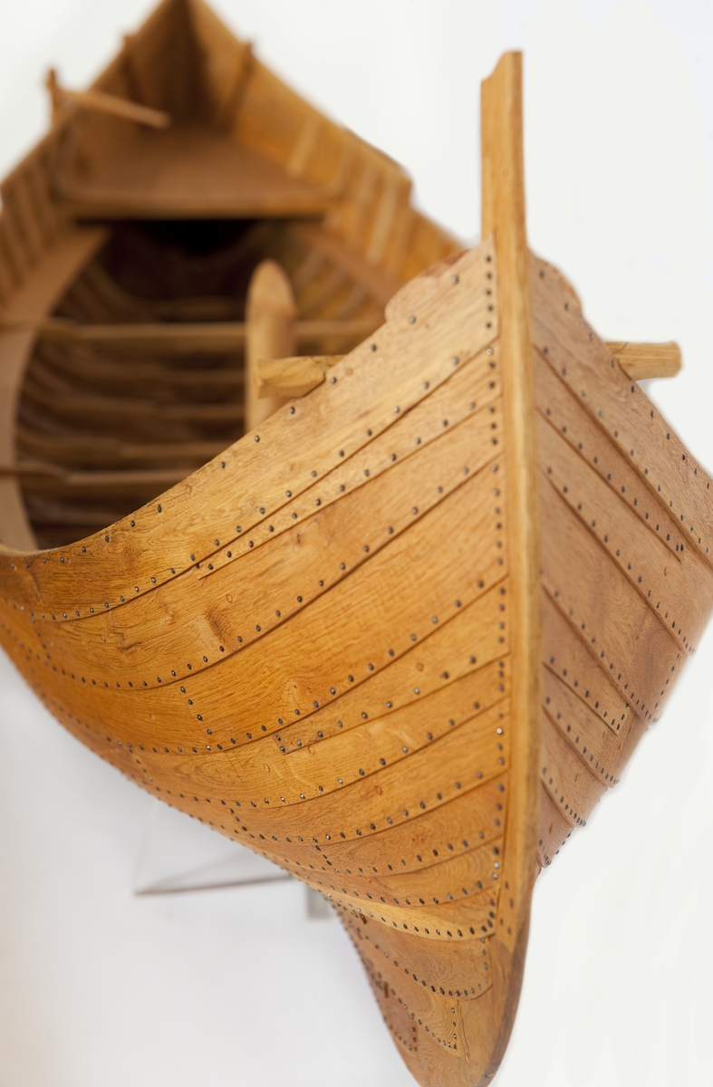 Fartygsmodell av ek, klinkbyggd på spant, högbordigt skepp (knarr)  ÄSKEKÄRRSBÅTEN  (fynd år 1933 fr. Göta älv, daterat 700 e. Kr.) Sidoroder på styrbordssidan, bordläggning förhöjd med ett bord i för- och akterskepp, liten back och halvdäck, kort kölsvin med mastspår.