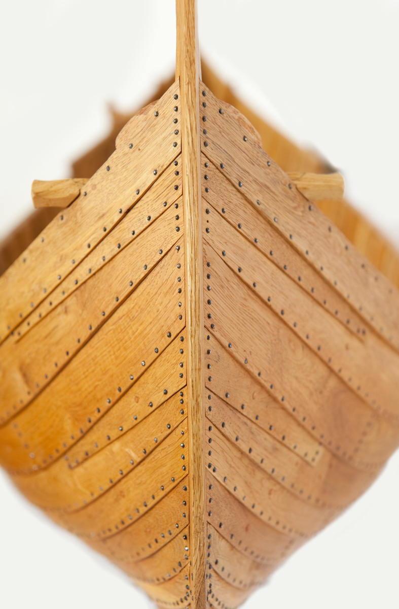 Fartygsmodell av ek, klinkbyggd på spant, högbordigt skepp (knarr)  ÄSKEKÄRRSBÅTEN  (fynd år 1933 fr. Göta älv, daterat 700 e. Kr.) Sidoroder på styrbordssidan, bordläggning förhöjd med ett bord i för- och akterskepp, liten back och halvdäck, kort kölsvin med mastspår.