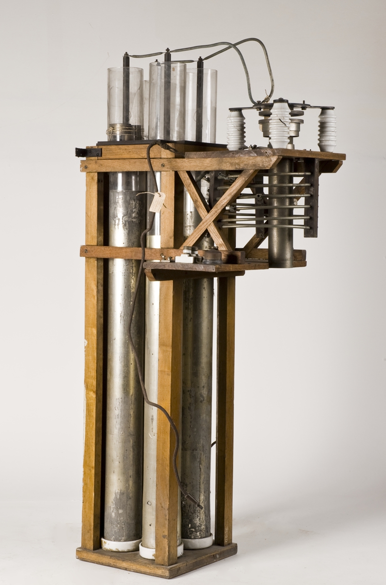 Radiosändare m/1906. Till en ställning av ek är monterad, dels 4 st långa, enkla leydnerflaskor, dels en galvaniserad avstämningsspole med få varv, dels en gniststräcka med porslinsisolatorer.
