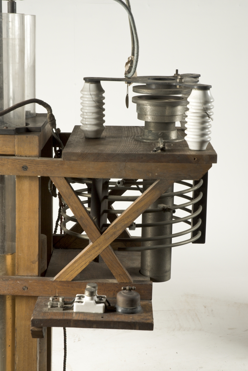 Radiosändare m/1906. Till en ställning av ek är monterad, dels 4 st långa, enkla leydnerflaskor, dels en galvaniserad avstämningsspole med få varv, dels en gniststräcka med porslinsisolatorer.