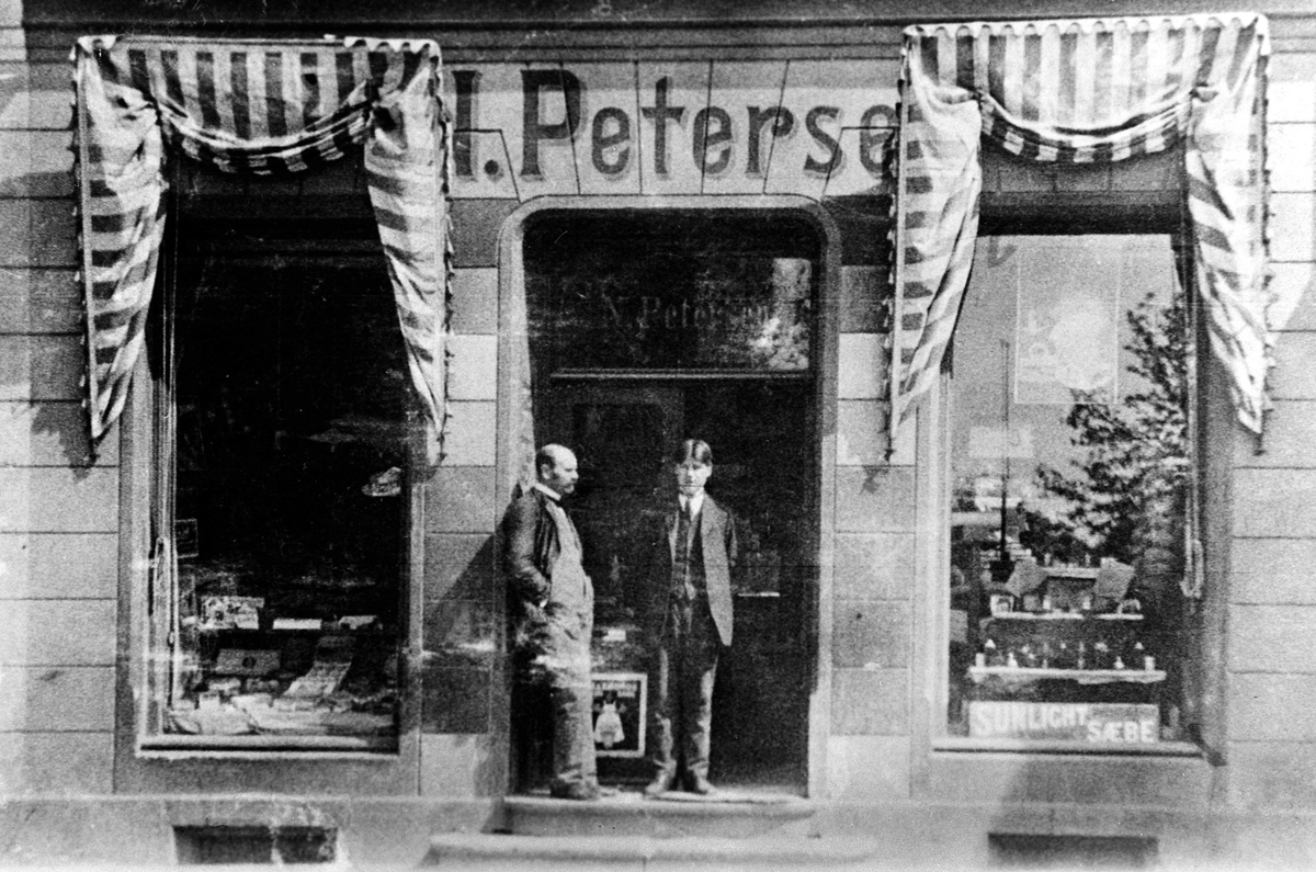 F. Petersens Fargehandel, Strandgata 53, Hamar. T.v. Filip Petersen, ukjent ekspeditør. Eksteriør, markiser.