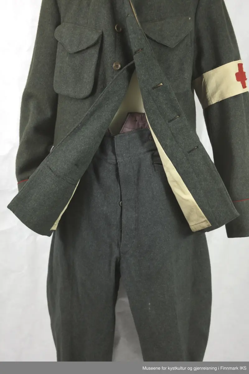 Uniformen besto opprinnelig av lue, jakke, bukse, belte og lærstøvler. Beltet og støvlene mangler. Uniformen består av mørkegrønn vadmel og har smale røde kanter ved yttersømmen til buksen, kragen og ved mansjettene. Luen / hatten har to parallelle gule striper rundt og på for- og baksiden. På fremsiden befinner seg en reim og et skjold som er svarte. På jakkens vestre armen er det festet en armbind med genferkors. Jakken lukkes med skjulte knapper i kunststoff . Den har to brystlommer og to sidelommer med klaff samt to metallhemper ved kragen. På innsiden til venstre befinner deg atter to lommer uten klaff. Jakken er foret med lyst, ubleket bomullsstoff. Den lange buksen er formet vid rundt lårbeinene, har to sidelommer og stropper nede. Den er en høy modell med knapper til seler og spensel i rygg. Buksen har en skult knepping i gylfen med metallknapper og en metallhempe øverst. Klærne er stemplet på innsidene.