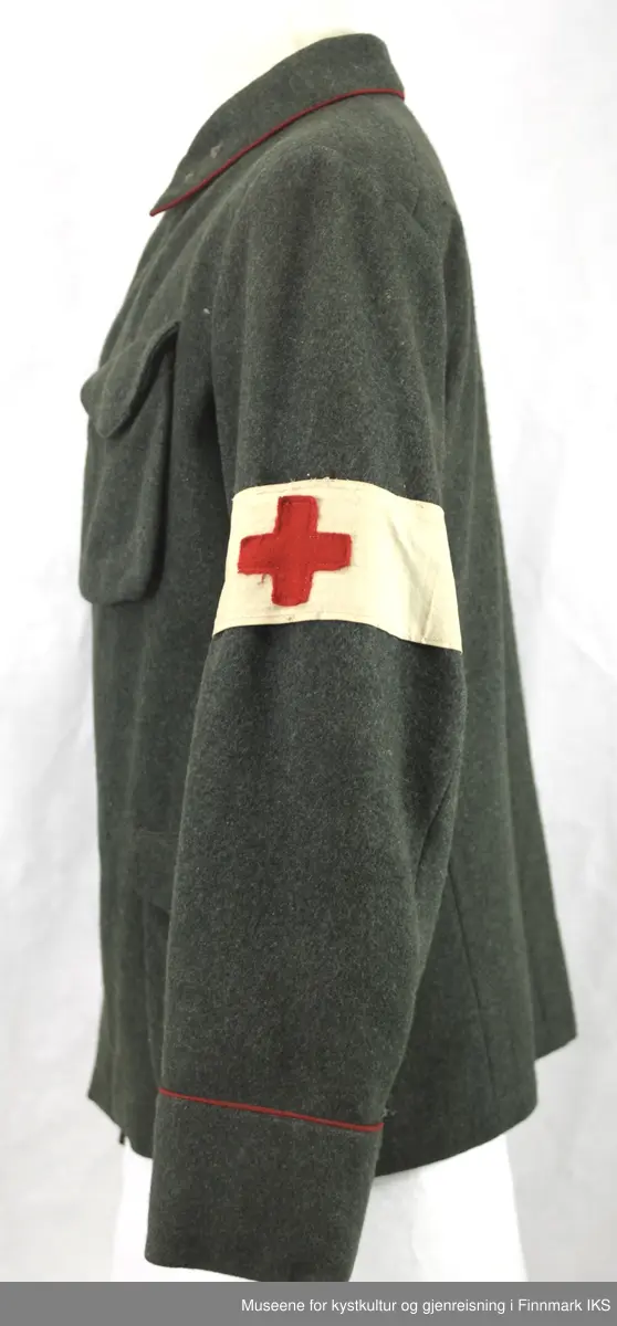 Uniformen besto opprinnelig av lue, jakke, bukse, belte og lærstøvler. Beltet og støvlene mangler. Uniformen består av mørkegrønn vadmel og har smale røde kanter ved yttersømmen til buksen, kragen og ved mansjettene. Luen / hatten har to parallelle gule striper rundt og på for- og baksiden. På fremsiden befinner seg en reim og et skjold som er svarte. På jakkens vestre armen er det festet en armbind med genferkors. Jakken lukkes med skjulte knapper i kunststoff . Den har to brystlommer og to sidelommer med klaff samt to metallhemper ved kragen. På innsiden til venstre befinner deg atter to lommer uten klaff. Jakken er foret med lyst, ubleket bomullsstoff. Den lange buksen er formet vid rundt lårbeinene, har to sidelommer og stropper nede. Den er en høy modell med knapper til seler og spensel i rygg. Buksen har en skult knepping i gylfen med metallknapper og en metallhempe øverst. Klærne er stemplet på innsidene.