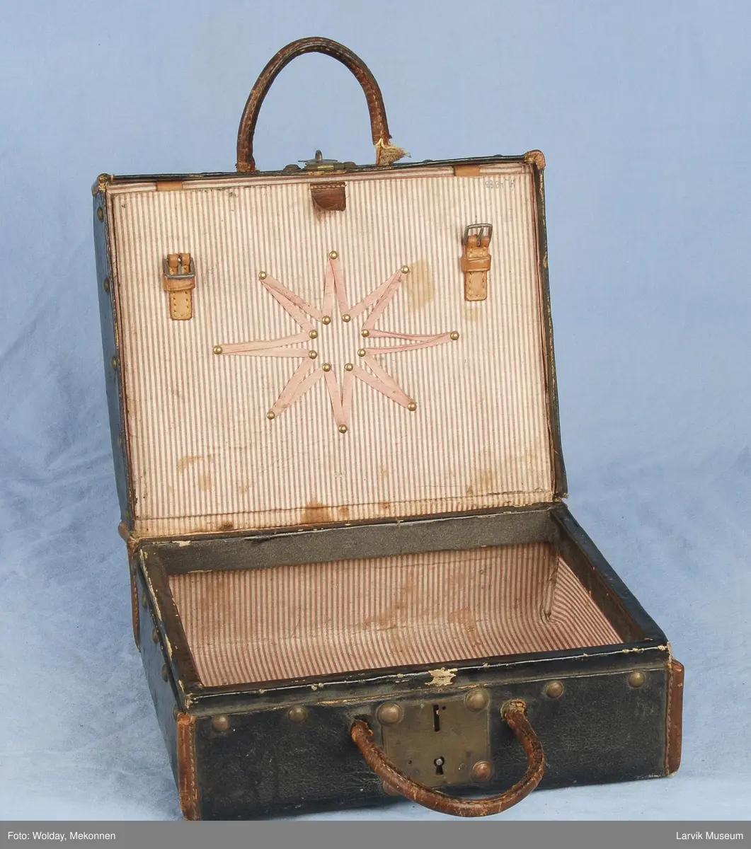 Form: Liten koffert med lås, buet håndtak på hver del. Inni er den delt i to med en plate som kan spennes fast med to stropper. Dekorert med metall kn
