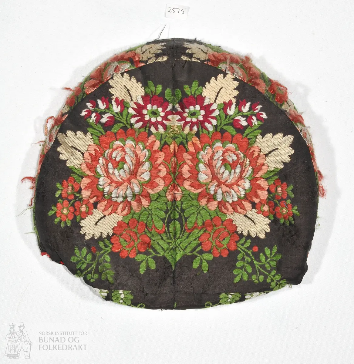 Botthuve i brosjert silke. Pull satt sammen av fire deler av stoffet. Vattert oppe og midt bak, men ikke nede ved rynkingen i nakken. Kantet med rosa silkeånd og foret med trykt, glansa bomull. Håndsøm. 

43,5cm