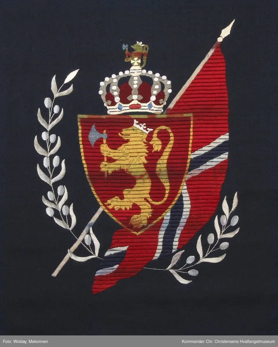 Den norske løve og det norske flagg med krone over, brodert i rødt, gult, gull, hvitt og blått. 
Det norske flagg med riksvåpen omkranset med to laubærgrener som symboliserer seier.