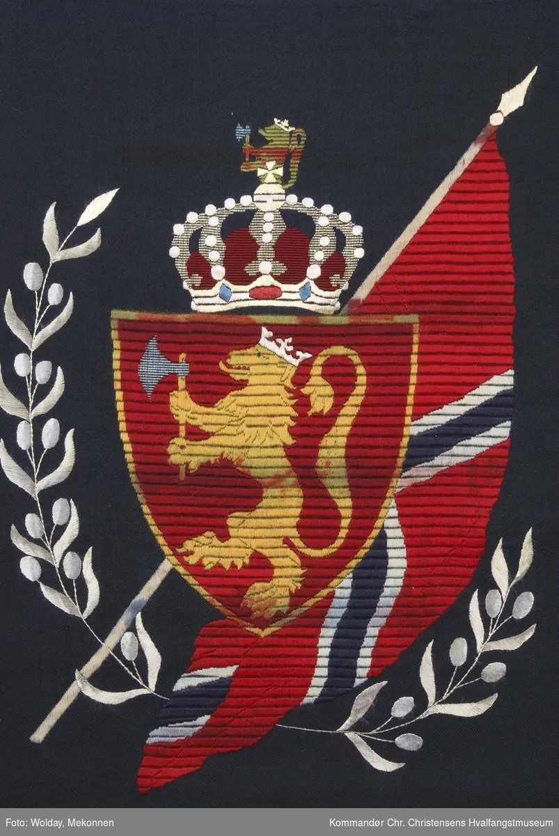 Den norske løve og det norske flagg med krone over, brodert i rødt, gult, gull, hvitt og blått. 
Det norske flagg med riksvåpen omkranset med to laubærgrener som symboliserer seier.