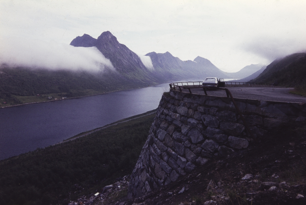 Fjord og fjell, fotografert fra vei i Gryllefjord. Bil parkert ved veien til høyre.