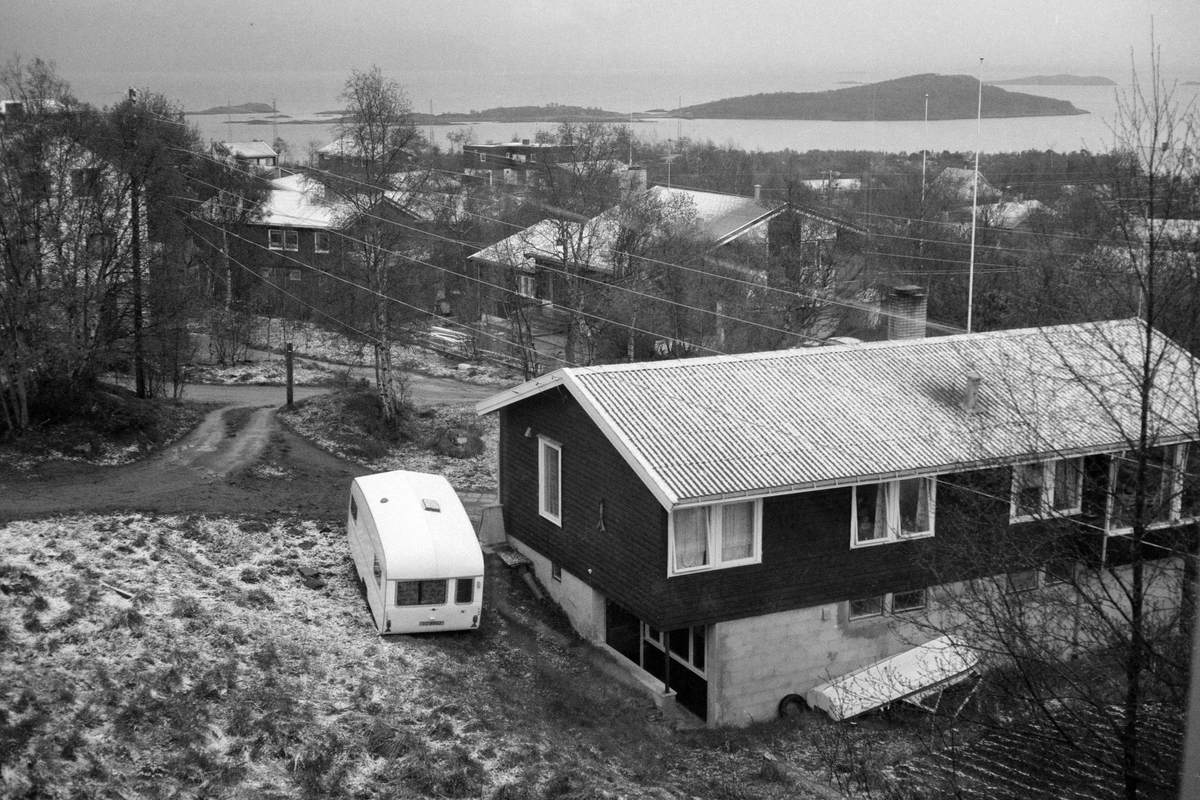 Campingvogn og hus, med hav og øyer i bakgrunnen. Snø på bakken.