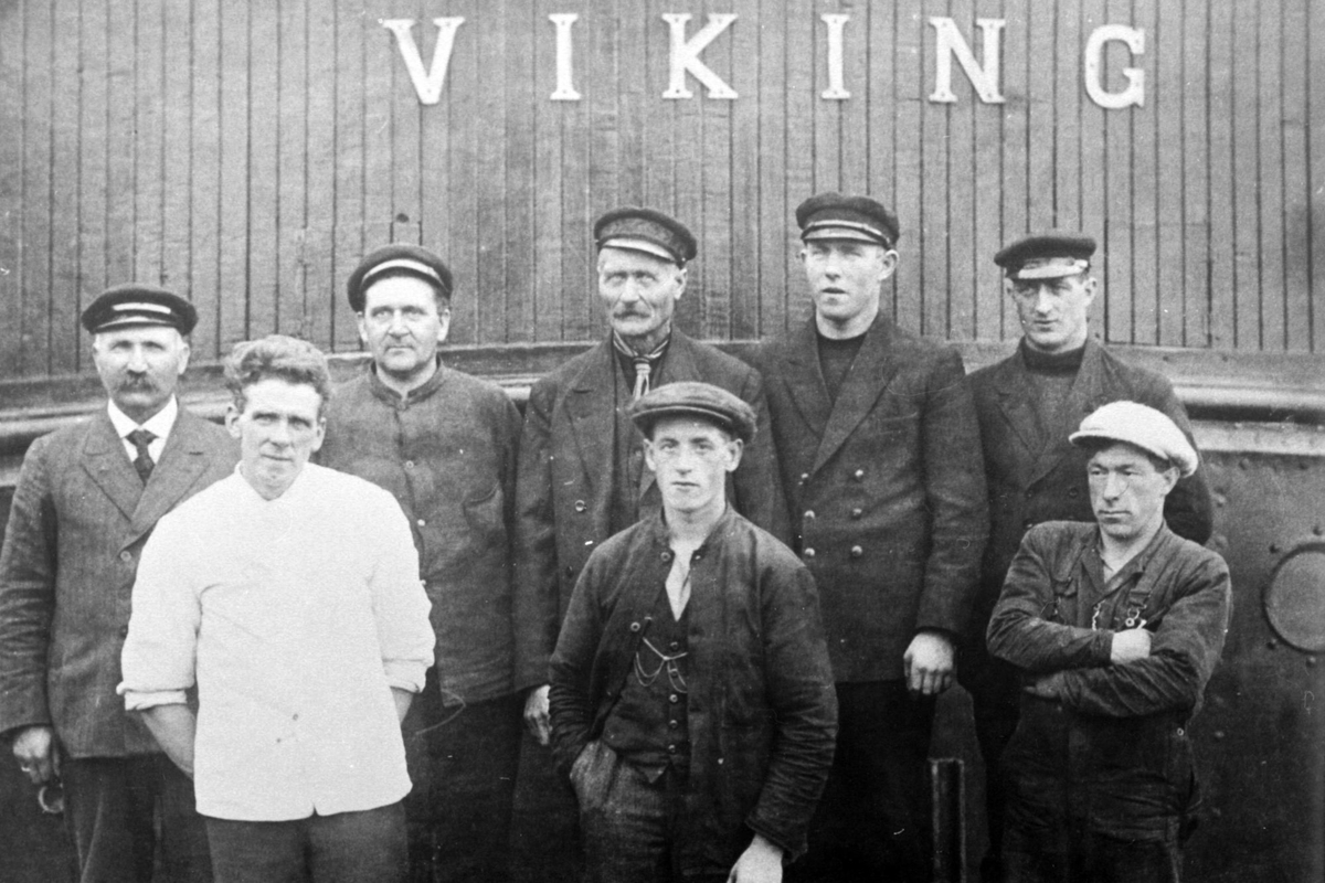 Gruppebilde av mannskapet på D/S "Viking", fotografert på dekk med skipsnavnet i bakgrunnen.