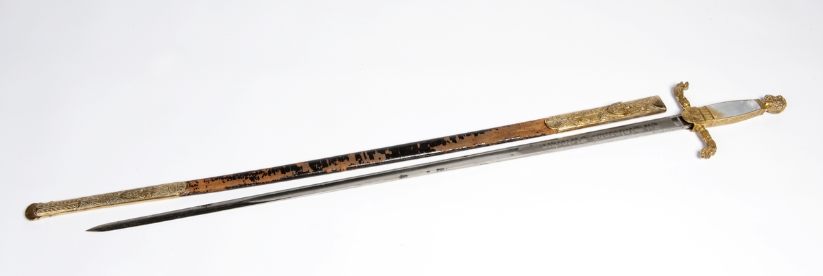 En kårde m/slire.  Dragehode som parerplate, krummet.  Gallakårde efter kaptein Palle Rømer Fleischer, perlemors håndtak 1ste repr for norsk jegerkorps.  Stål m/messingbeslag.  Sliren i skinn med messingbeslag, løvemerke.  Skjeftet m/visirhode.
