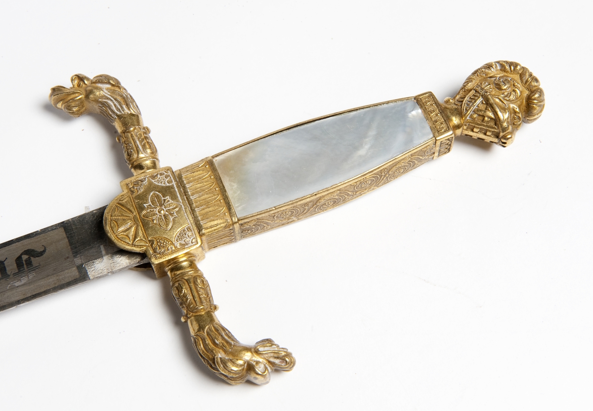 En kårde m/slire.  Dragehode som parerplate, krummet.  Gallakårde efter kaptein Palle Rømer Fleischer, perlemors håndtak 1ste repr for norsk jegerkorps.  Stål m/messingbeslag.  Sliren i skinn med messingbeslag, løvemerke.  Skjeftet m/visirhode.