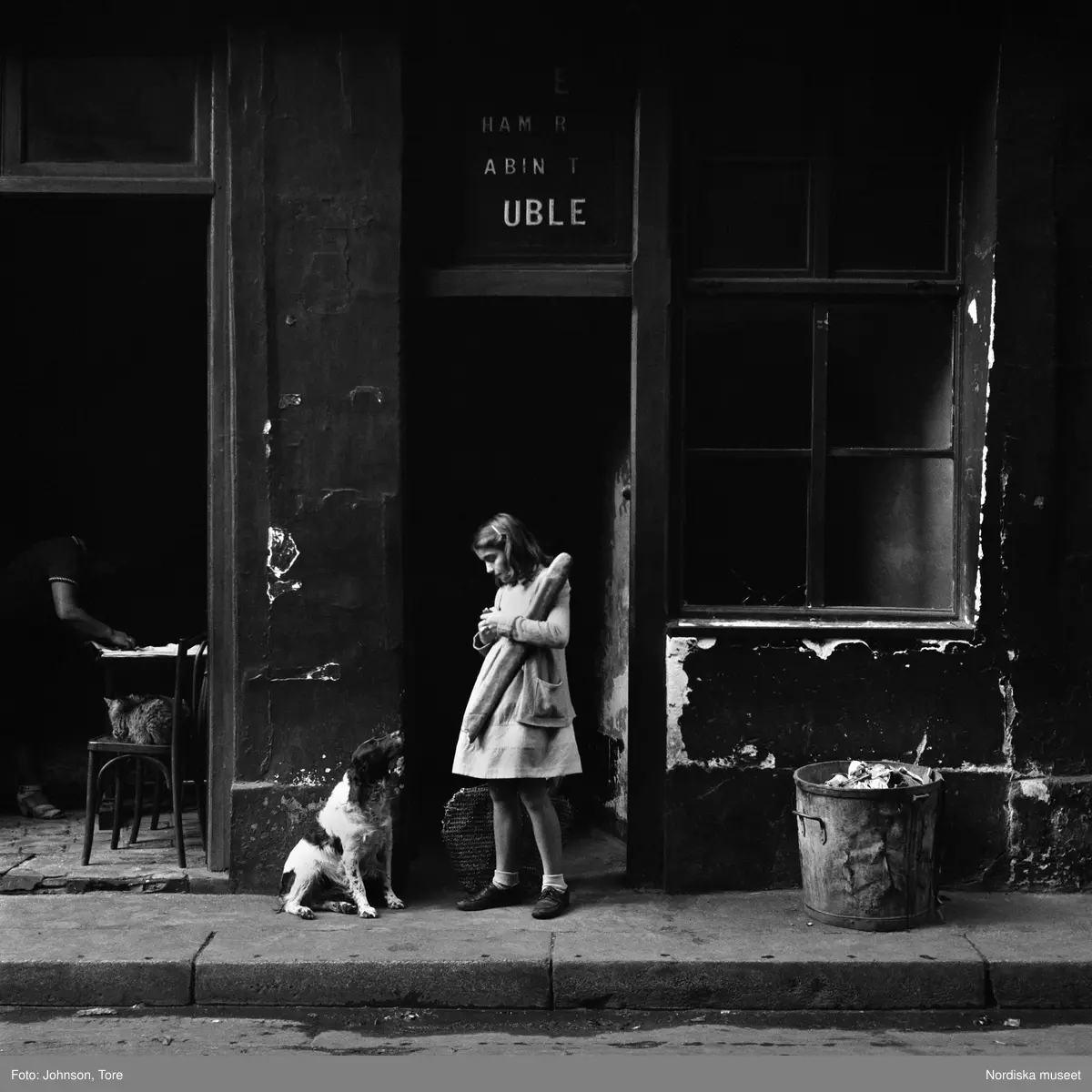 Flicka och hund på trottoar i Paris. Flickan håller i ett långt bröd.