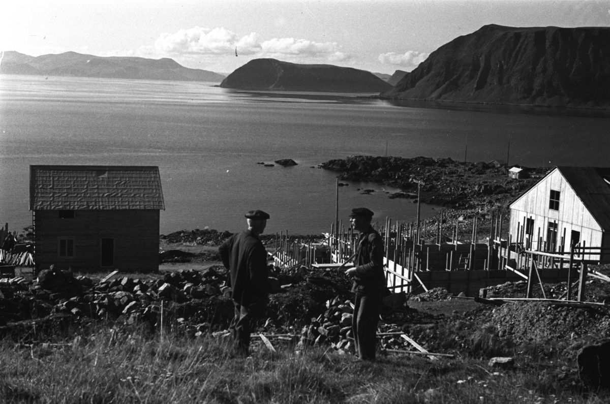 To menn slår av en prat ovenfor noen gjenreisningsbygg i Honningsvåg.

Arkitekt Ola Hanche-Olsen arbeidet ved Brente Steders Reguleringskontor i 1946. Hovedadministrasjon for gjenreisning av Nord-Troms og Finnmark ble lagt til Harstad og fikk navnet Finnmark kontoret. Landsdelen Nord-Troms og Finnmark blev oppdelt i syv distrikt med hver sin administrasjon. Honningsvåg, distrikt IV, skulle betjene Nordkapp, Lebesby, Porsanger og Karasjok kommune.

Ola Hanche-Olsen har tatt bildene. Han var født 13. mars 1920 i Borre, død 11. februar 1998 i Gjettum. Han var både arkitekt og barnebokforfatter. Han hadde artium fra 1939, arkitekteksamen fra NTH 1946 og arbeidet deretter ved Finnmarkskontoret 1946–48 før han etablerte egen arkitektpraksis. Han debuterte som barnebokforfatter i 1974 med lettlest-boka "Knut og sjørøverne", og skrev i alt 12 bøker. Han var XU-agent 1944-45, og var også en aktiv fjellklatrer og friluftsmann. Ola var gift med Solveig Hanche-Olsen (f. Falkenberg); de fikk 3 barn, blant dem matematikeren Harald Hanche-Olsen.

