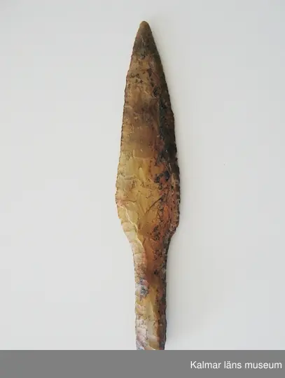 KLM 552. Dolk. Av gulbrun flinta. Senneolitisk tid. Bladet är parallellhugget och insvängt ned mot skaftet. Oskadad. Äldre märkning: A 189 I.