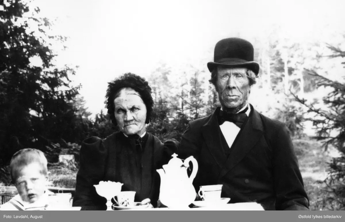 Engebret Hansen og Nikoline Abrahamsdatter Haugane, fra Haugane i Ullerøy, Skjeberg med datter og hennes sønn, 1898. Husmannsplass under gården Lileng østre. De hadde fire barn: Johan, Hans, Hanna og Elen. Hanna ble født 1862 og Elen i 1867. Det kan være Lene eller Hanna som er på bildet, og hennes sønn.
Det var flere brn i familien. 
Det vises også et utsnitt av bildet. 

Ifølge folketelling 1891 for Skjeberg drev Engebret : "Skrædderhåndværk for egen Regning og Pladsbrug som Husmand".